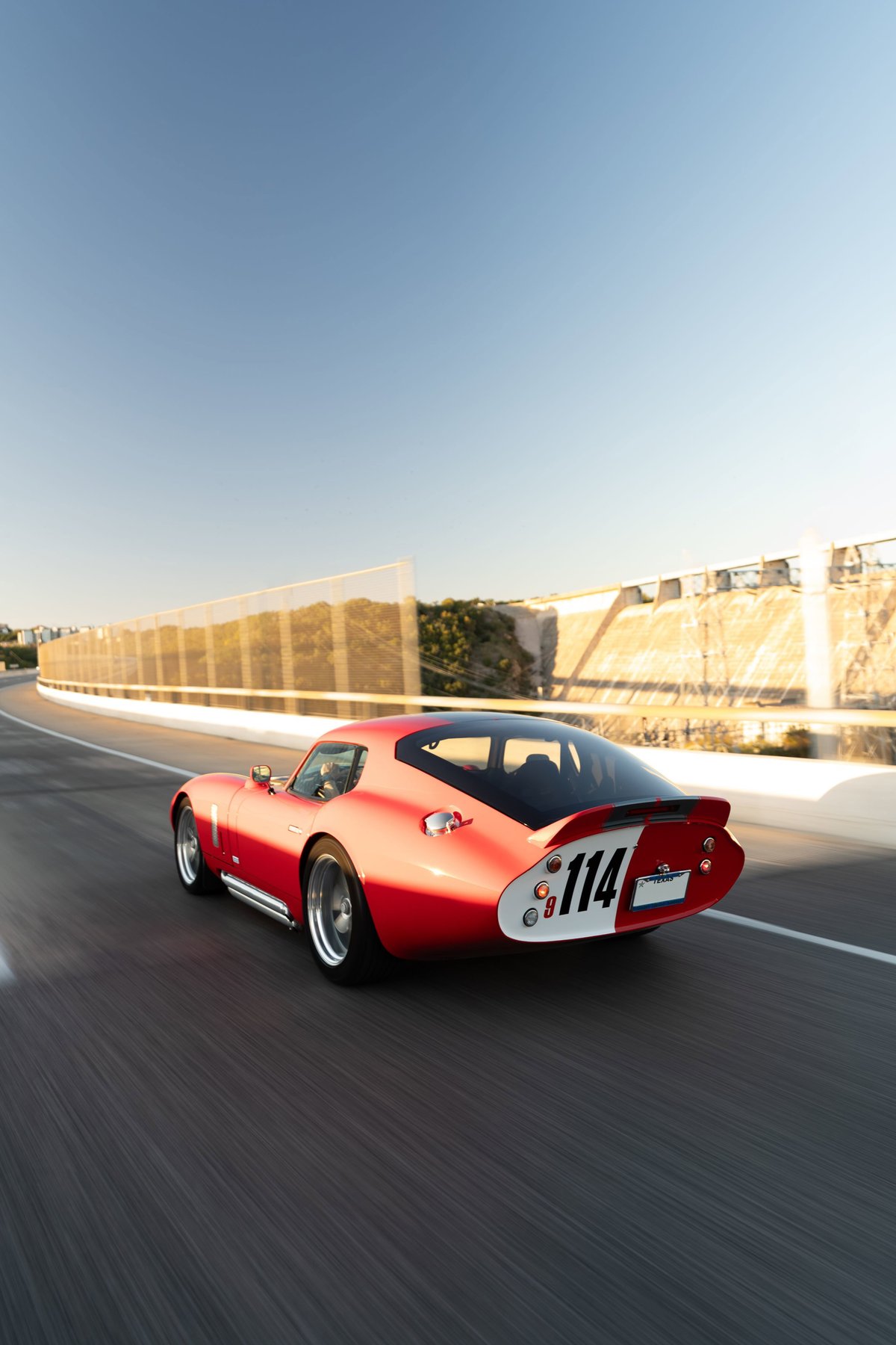 Rear view of a red 1965 Superformance Shelby Daytona CSX with racing livery #114 and polished rims.