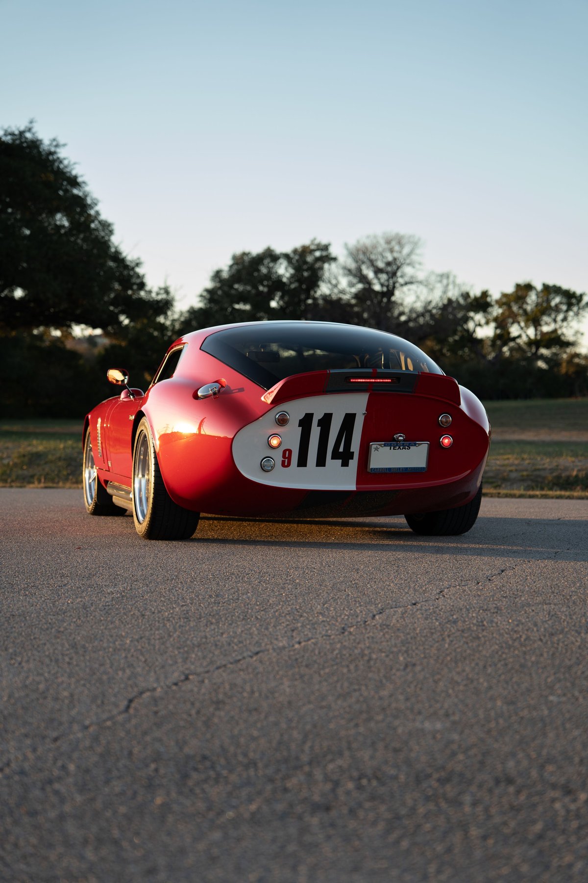 Rear view of a red 1965 Superformance Shelby Daytona Coupe with a racing livery and #114.