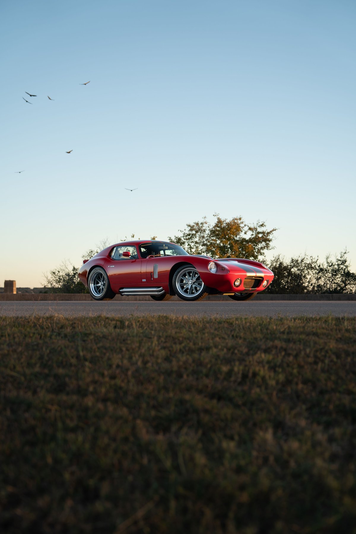 Red 1965 Superformance Shelby Daytona CSX coupe with racing stripes and chrome exhaust pipes.