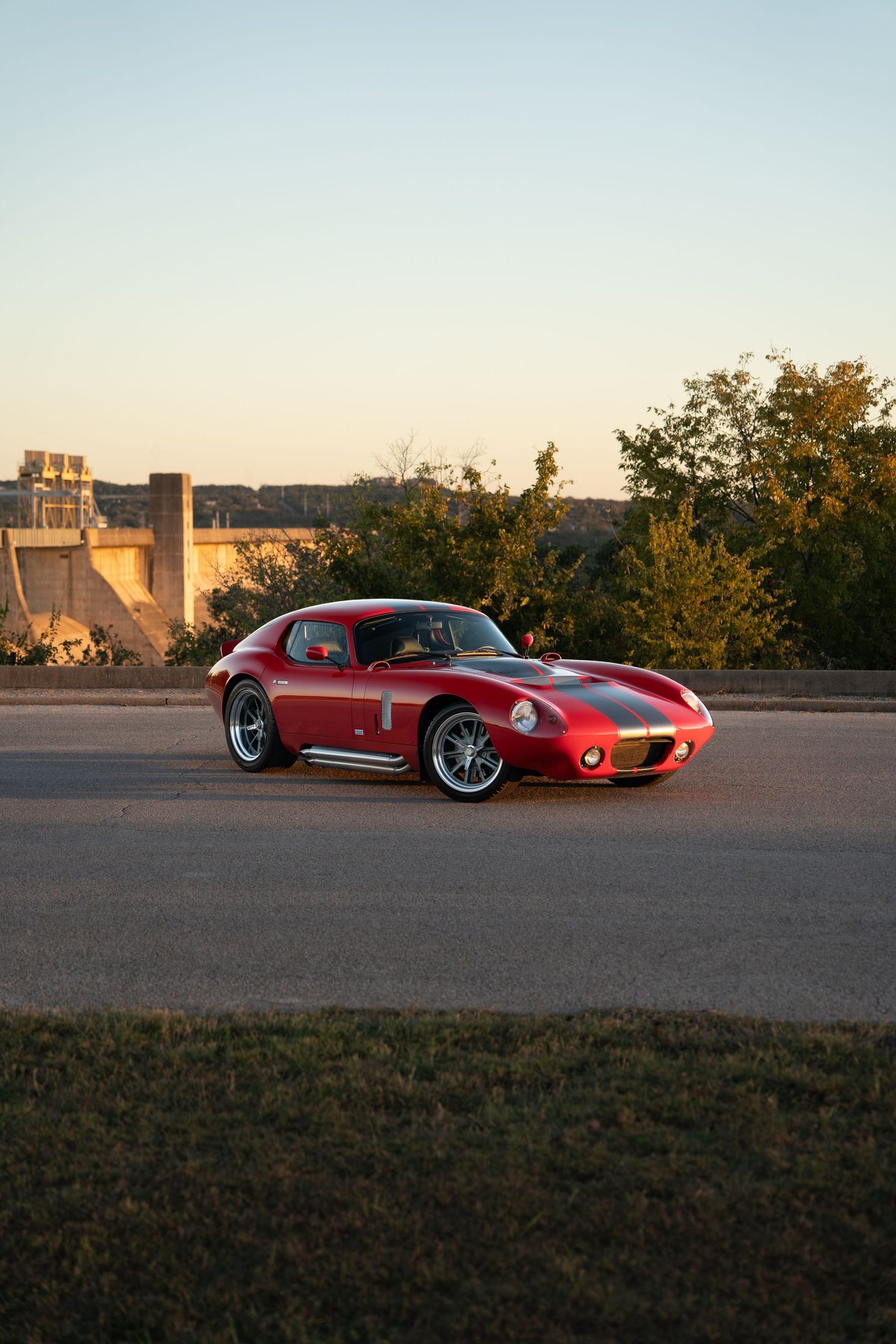 Red 1965 Superformance Shelby Daytona CSX with black racing stripes, chrome side pipes, and alloy rims.