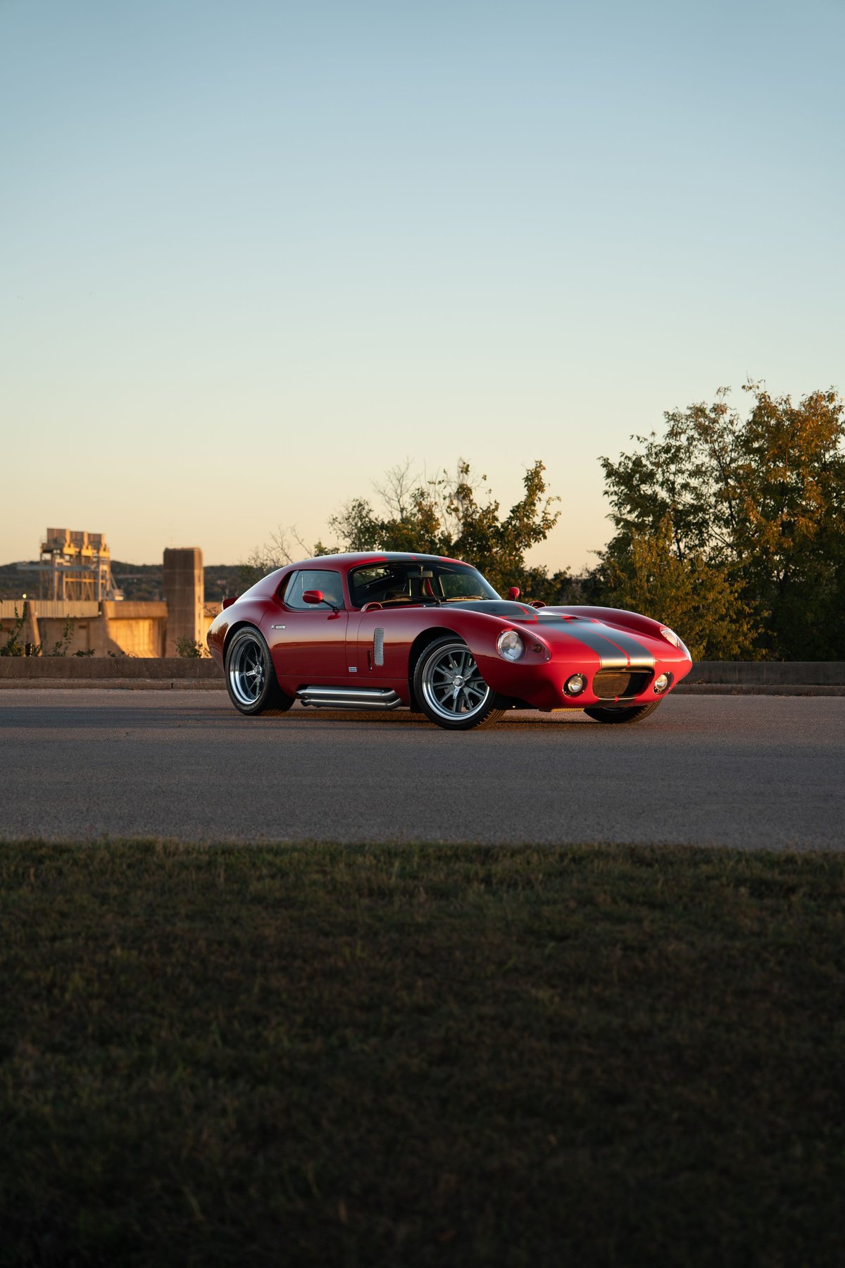 A red 1965 Superformance Shelby Daytona CSX with dual racing stripes on the hood, and chrome side pipes.