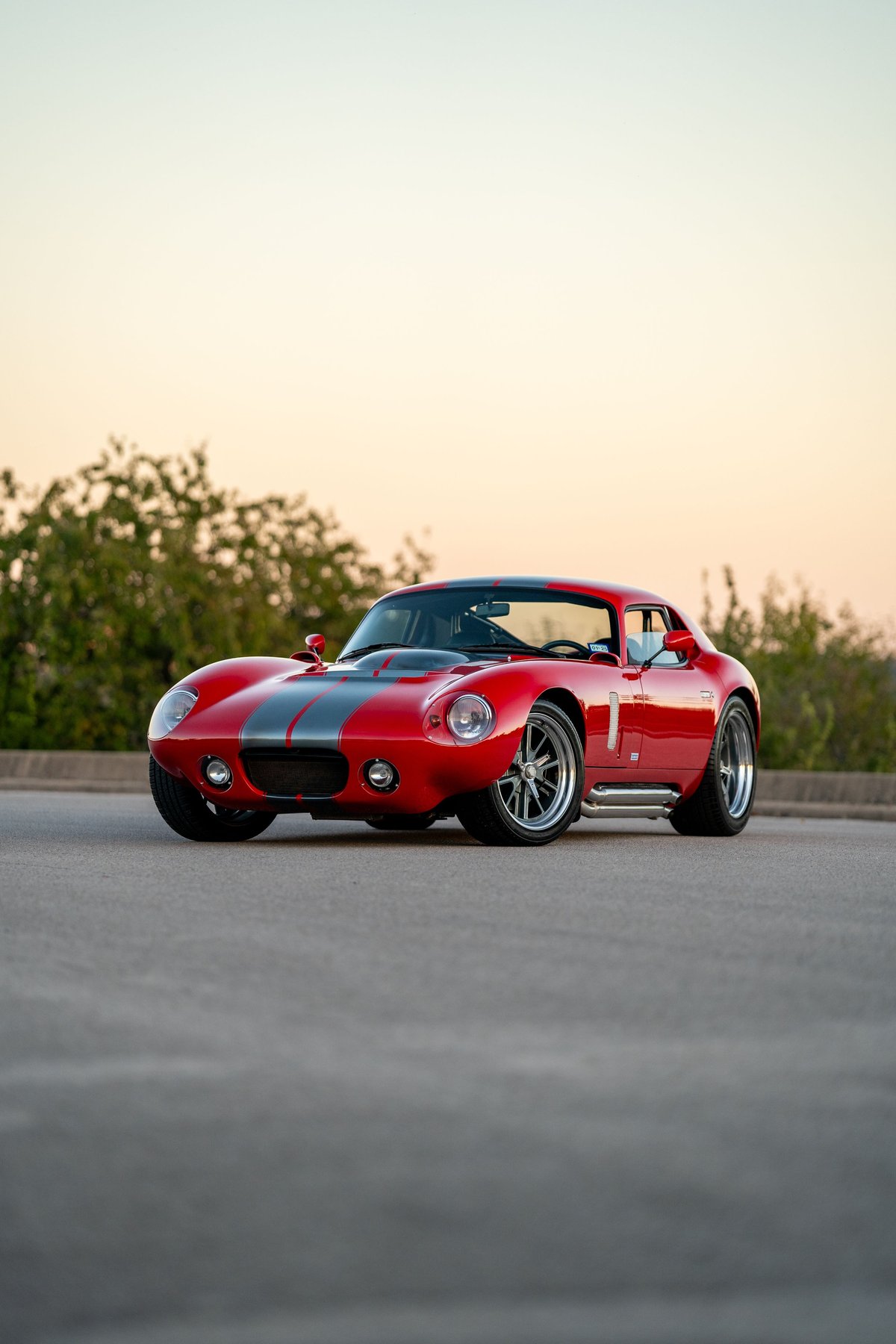 Red 1965 Superformance Shelby Daytona coupe with grey racing stripes and chrome rims.