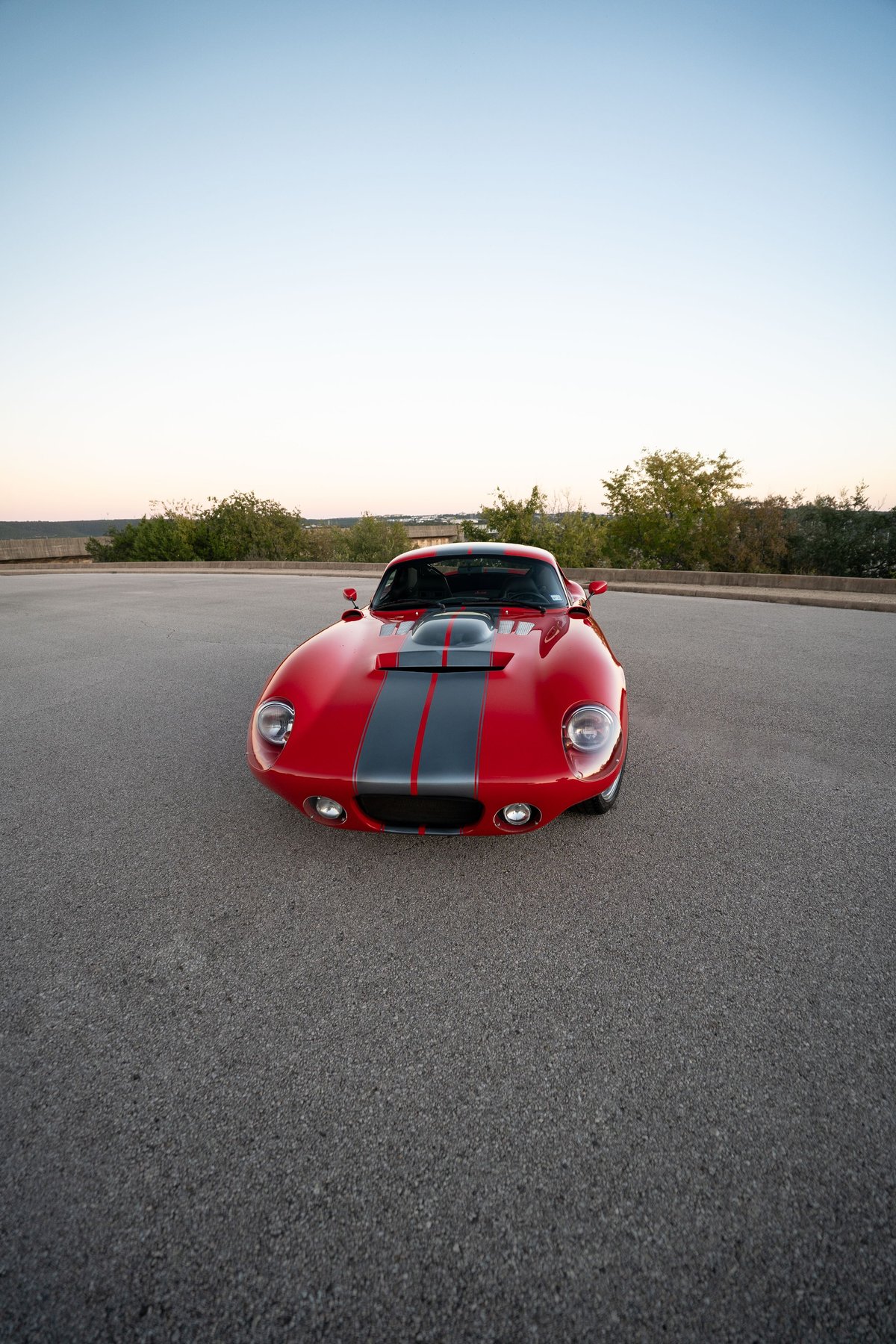 Red 1965 Superformance Shelby Daytona Coupe with dual gray racing stripes and a hood scoop.