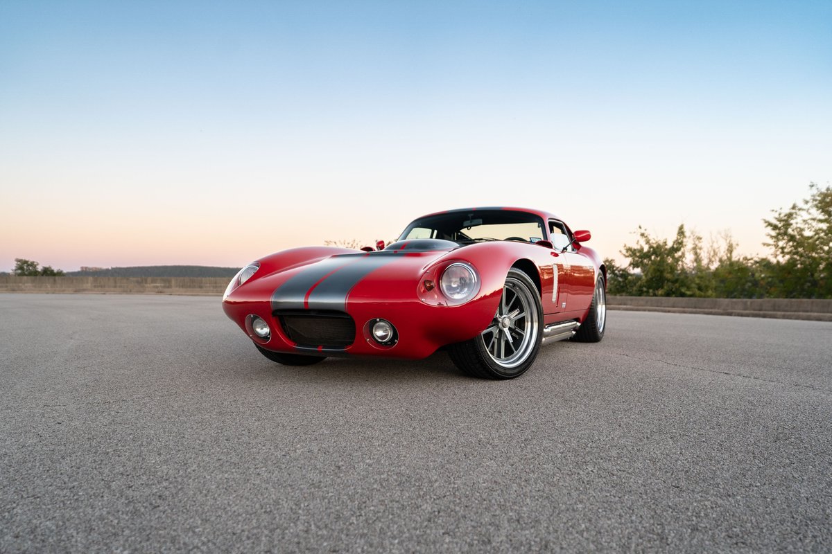 Red 1965 Superformance Shelby Daytona Coupe with dual grey racing stripes and chrome rims.