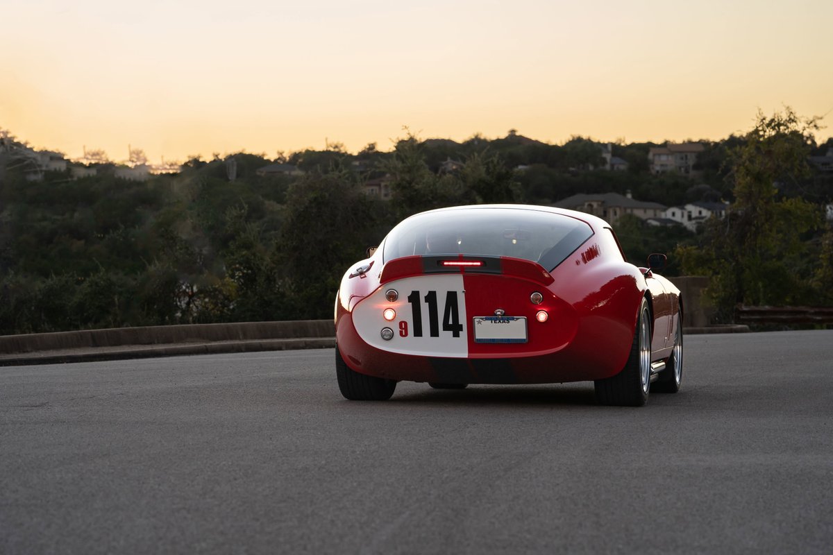 Rear view of a red 1965 Superformance Shelby Daytona coupe with racing livery #114 and chrome rims.