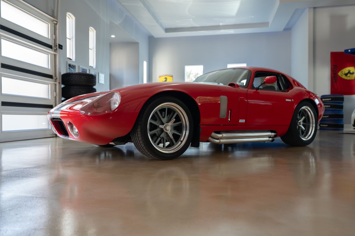 Low angle shot of a red 1965 Superformance Shelby Daytona Coupe with polished side pipes and alloy rims.