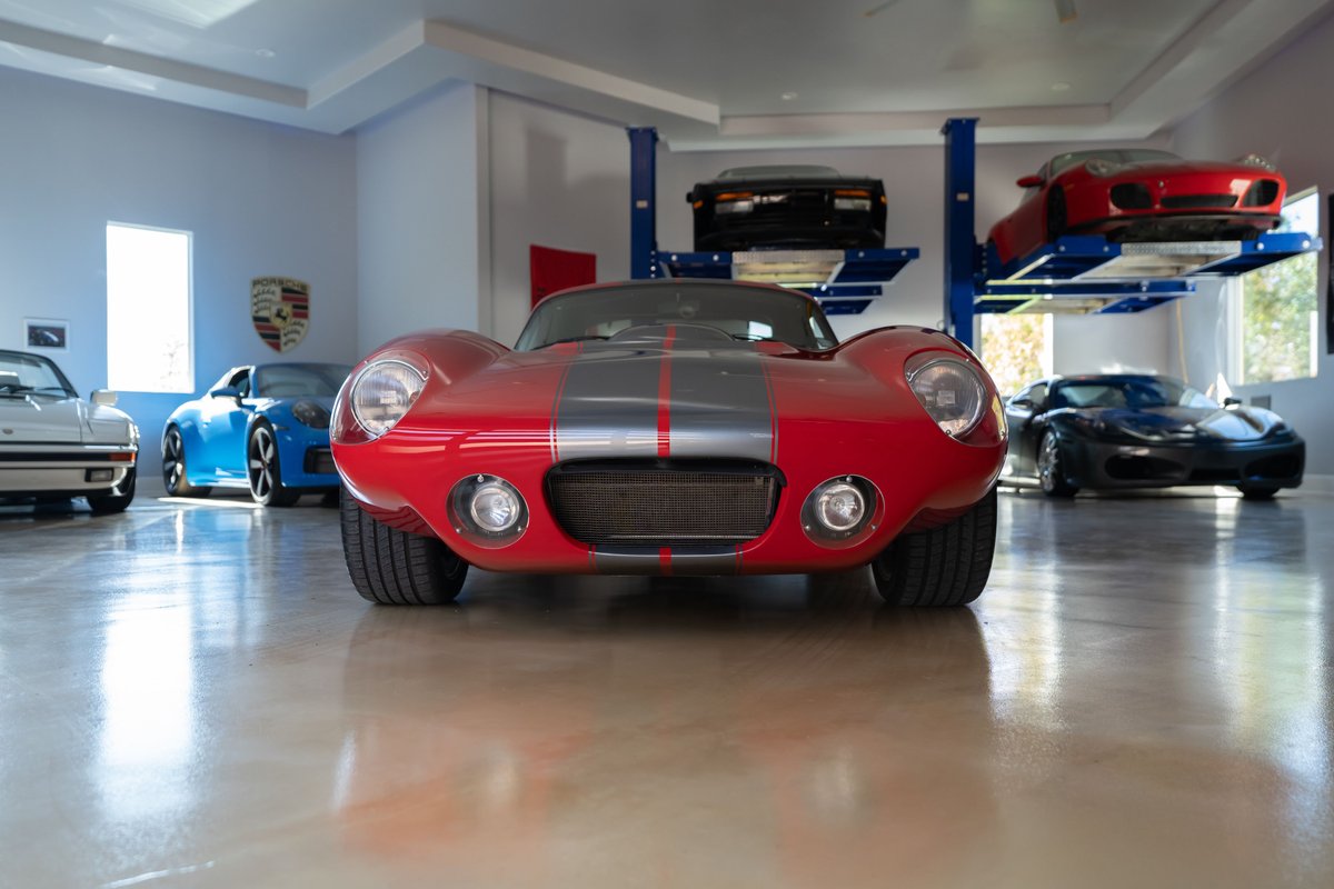 Red 1965 Superformance Shelby Daytona CSX with dual gray racing stripes and chrome rims.