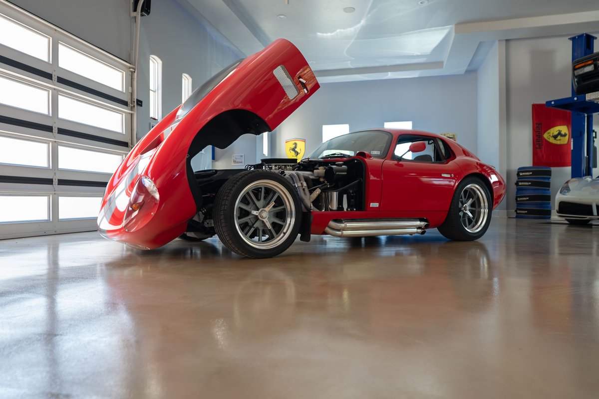 Red 1965 Superformance Shelby Daytona coupe with hood open, showcasing its engine and chrome side pipes.