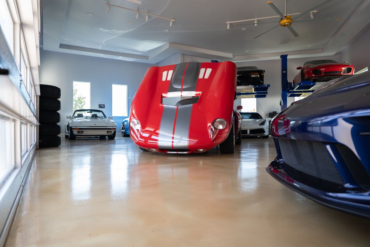 Red 1965 Superformance Shelby Daytona Coupe with silver racing stripes and a blue car in the foreground.
