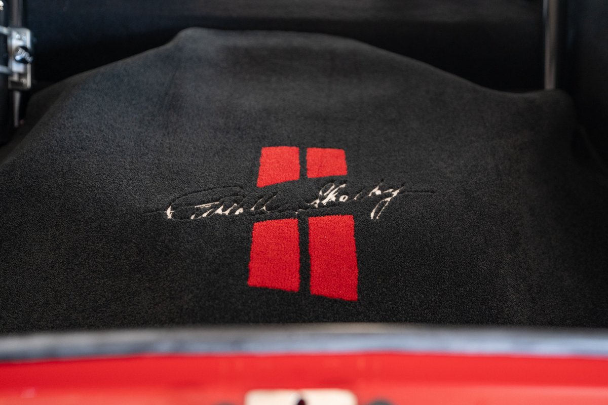Black floor mat with red Shelby Cobra emblem and signature in a red 1965 Superformance Shelby Daytona Coupe.