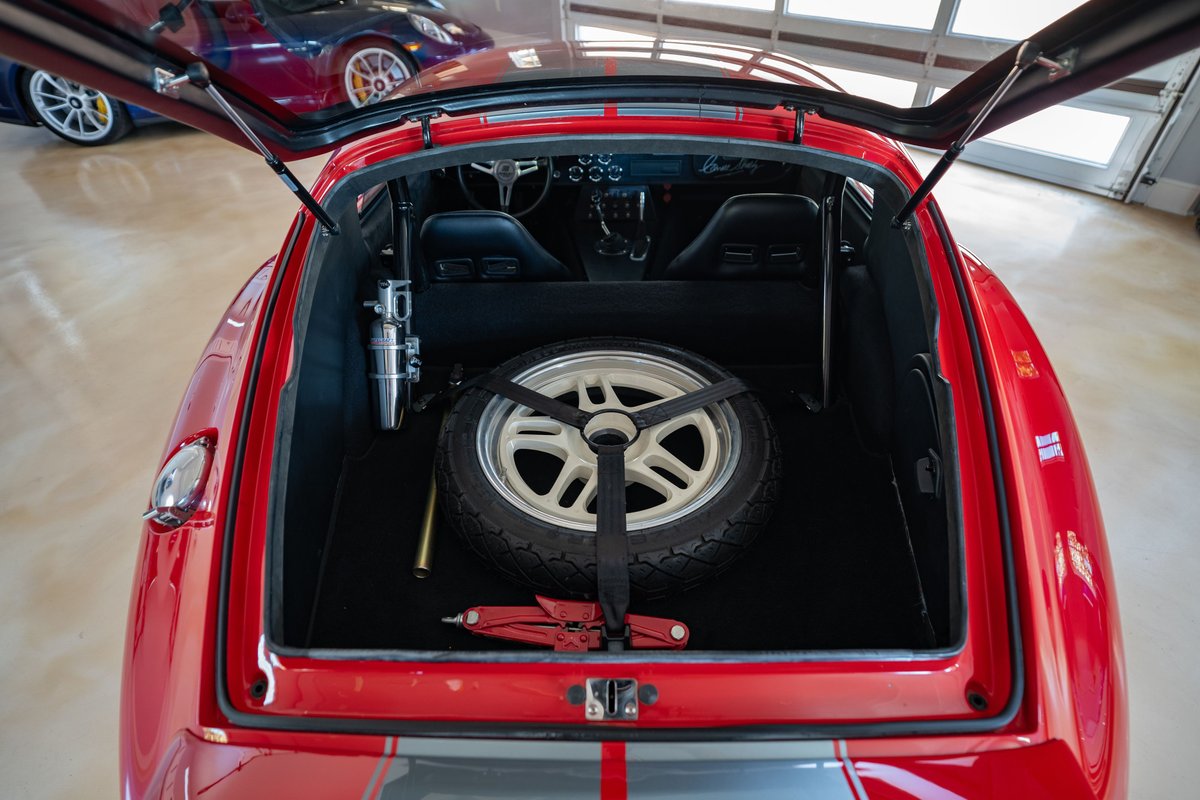 Red 1965 Superformance Shelby Daytona with spare tire, jack, and racing seats in trunk.