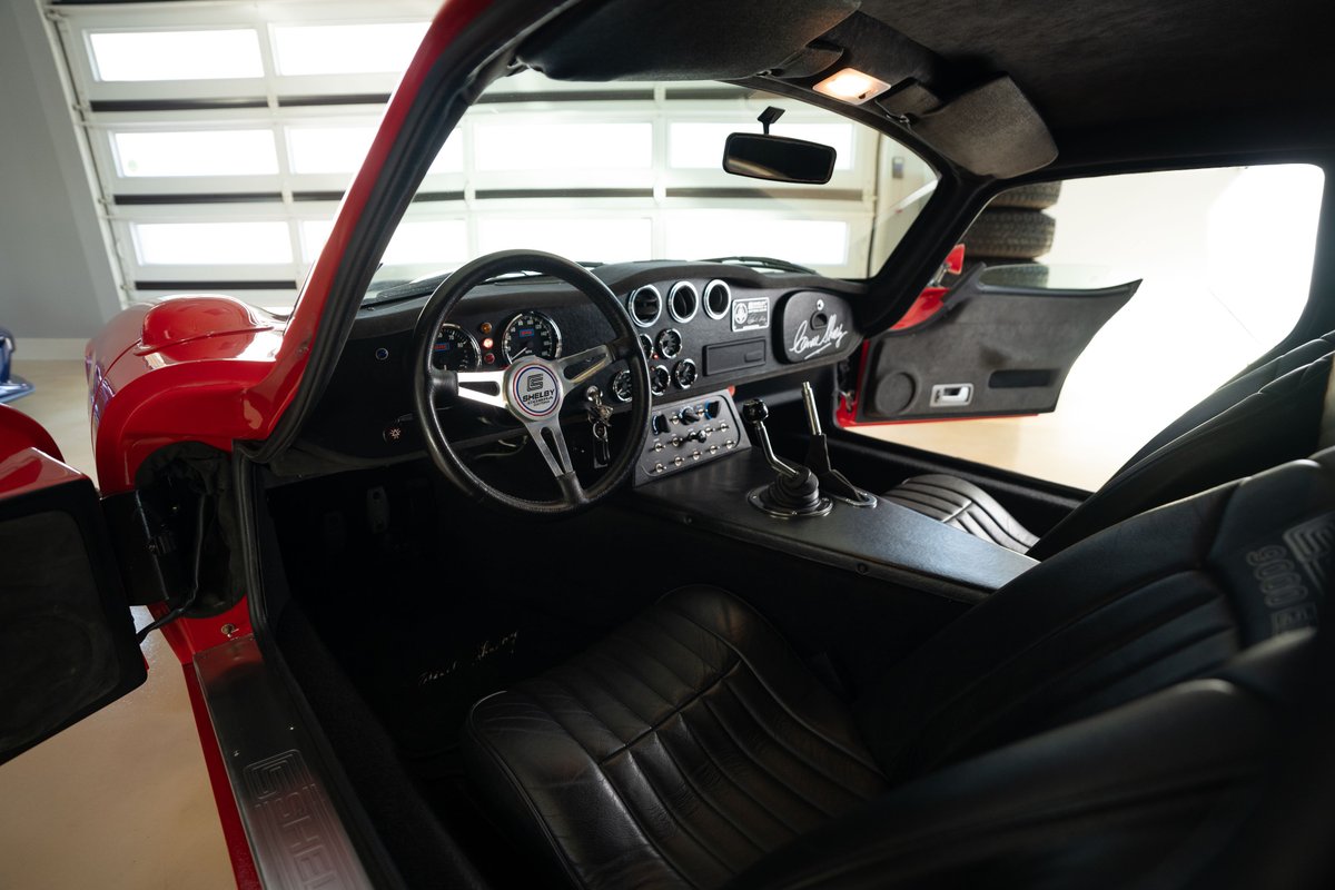 Interior view of a red 1965 Superformance Shelby Daytona Coupe with black leather seats and dashboard.