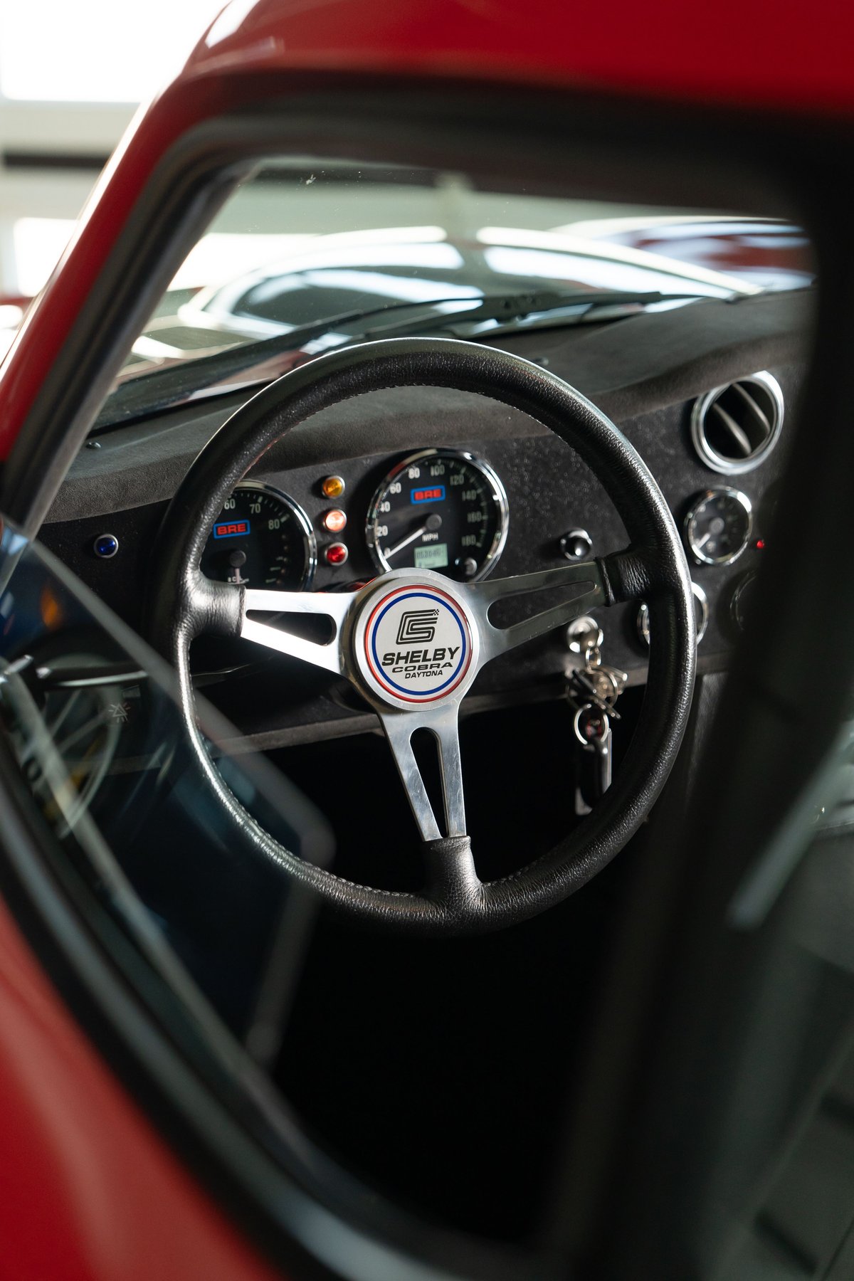 Close-up of a Shelby Daytona CSX steering wheel and dashboard. Red exterior paint is visible.