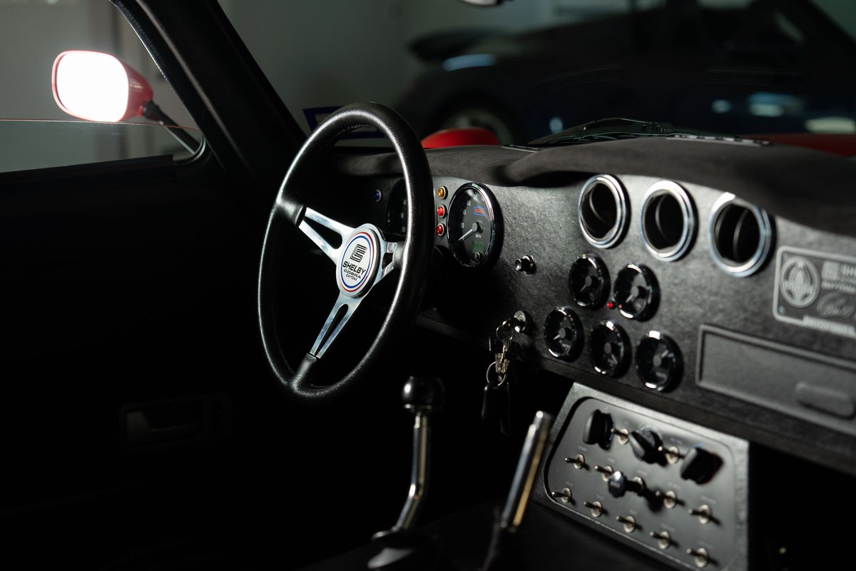 Interior of a Monza Red 1965 Superformance Shelby Daytona CSX, featuring a vintage steering wheel and dashboard gauges.