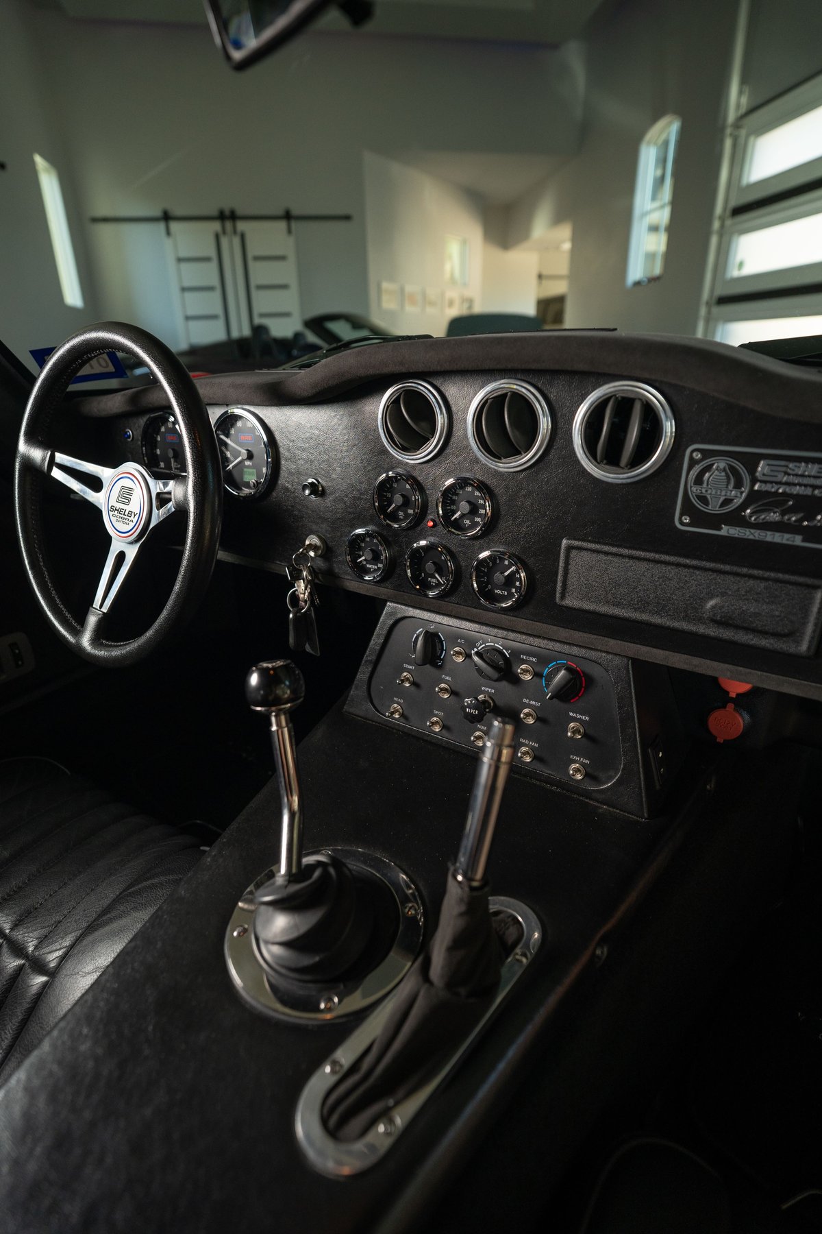 Interior of a red 1965 Superformance Shelby Daytona CSX showing the steering wheel, gauges, and dual shifters.