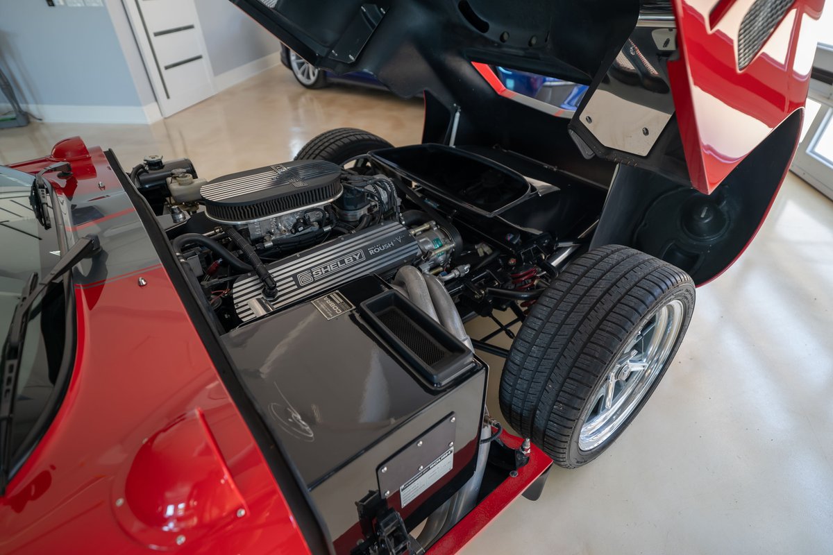 Red 1965 Superformance Shelby Daytona coupe with exposed V8 engine and chrome rims.