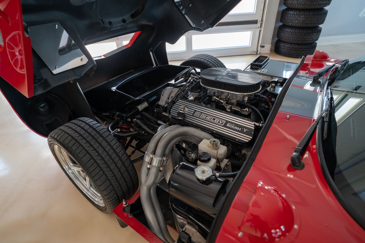 Red 1965 Shelby Daytona CSX with open hood, revealing a Shelby 427 V8 engine and chrome rims.