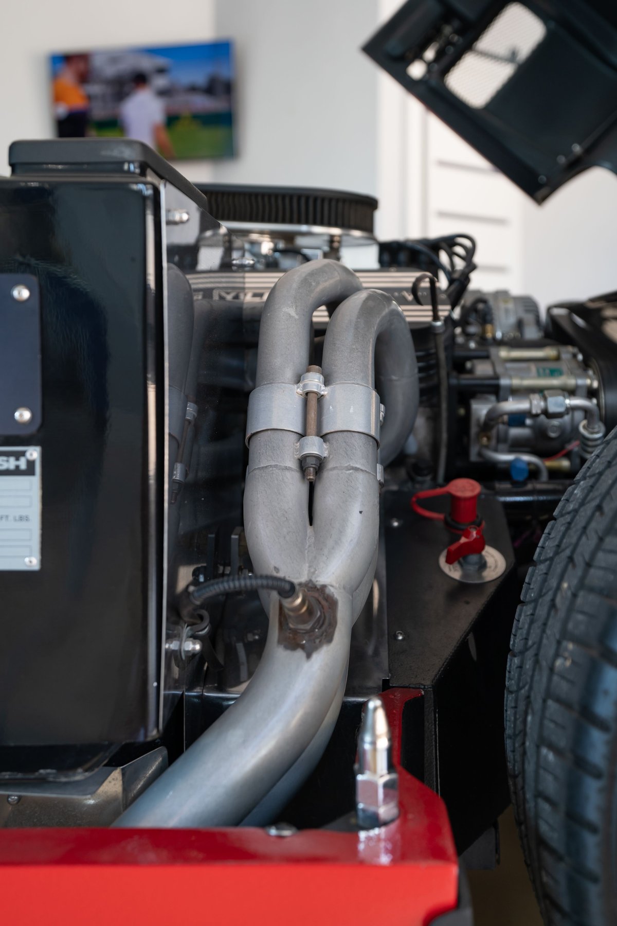 Close up of Monza Red 1965 Superformance Shelby Daytona's engine bay, showing exhaust headers and tire.