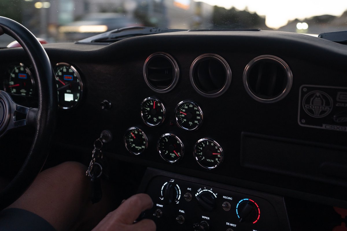 Interior of a Monza Red 1965 Superformance Shelby Daytona CSX, showing dashboard gauges and steering wheel.