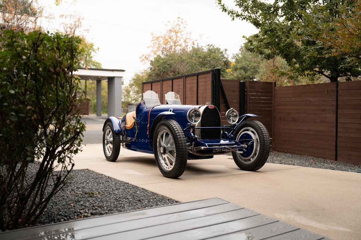 A blue 1927 Bugatti Type 35 Pur Sang race car with chrome rims and spoked wheels.