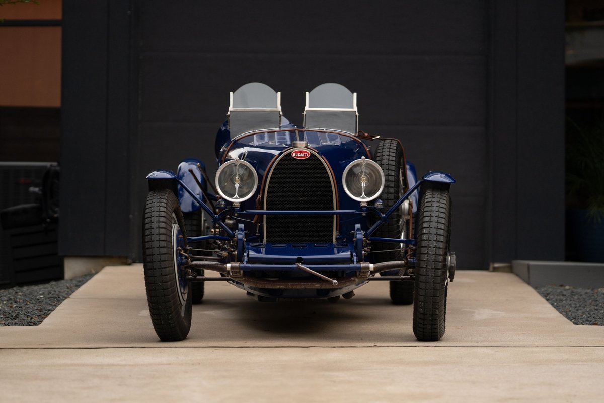 Front view of a blue 1927 Bugatti Type 35 Pur Sang, with exposed rims and twin windscreens.