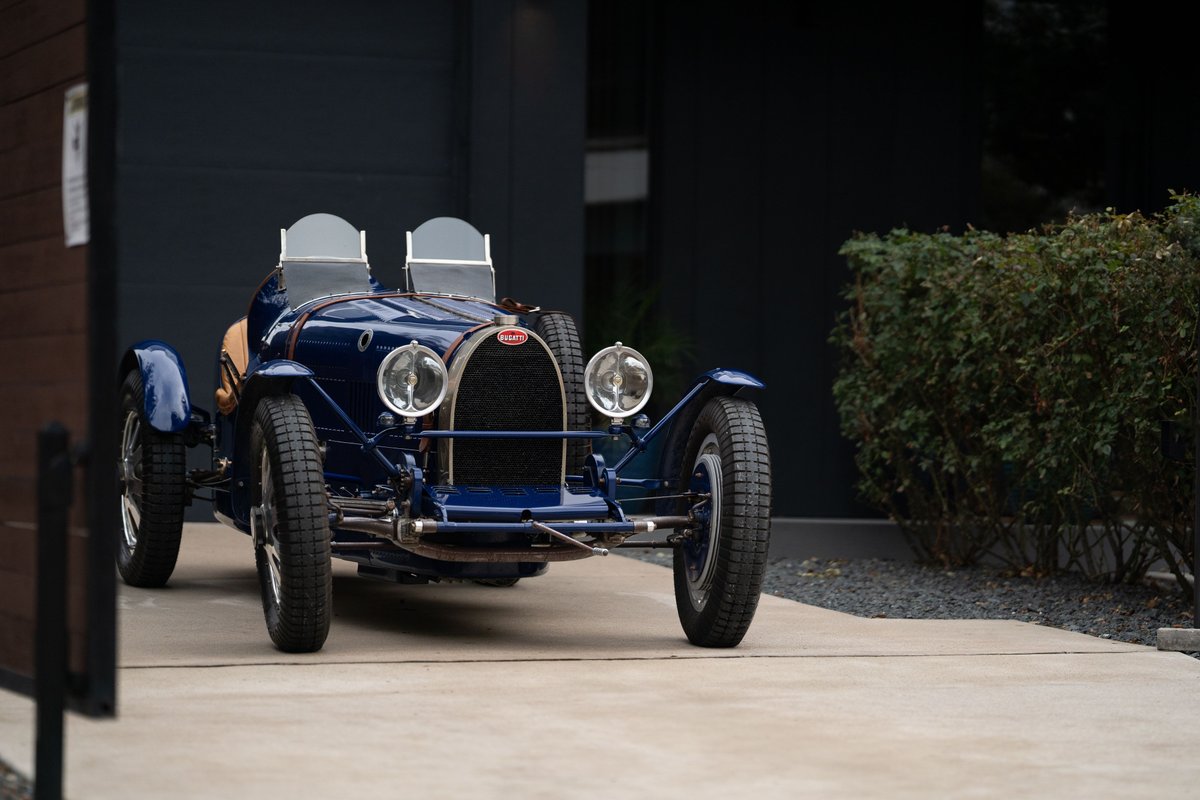 A blue 1927 Bugatti Type 35 Pur Sang roadster with exposed wire wheels and dual windscreens.