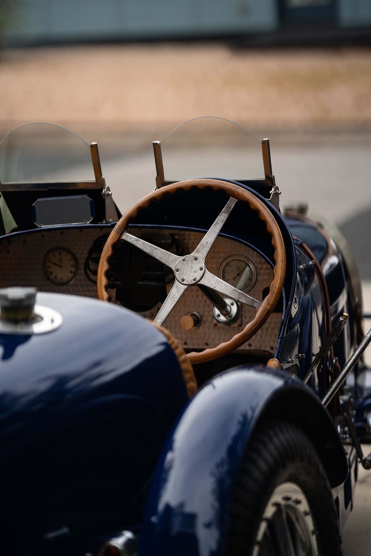 Close-up of a vintage blue 1927 Bugatti Type 35 dashboard with a wooden steering wheel and gauges.