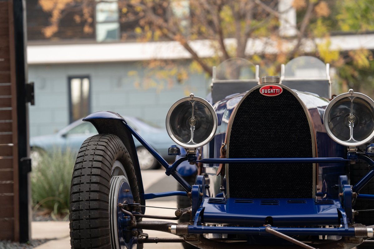 Front view of a blue 1927 Bugatti Type 35 Pur Sang with mesh grille and iconic Bugatti emblem.