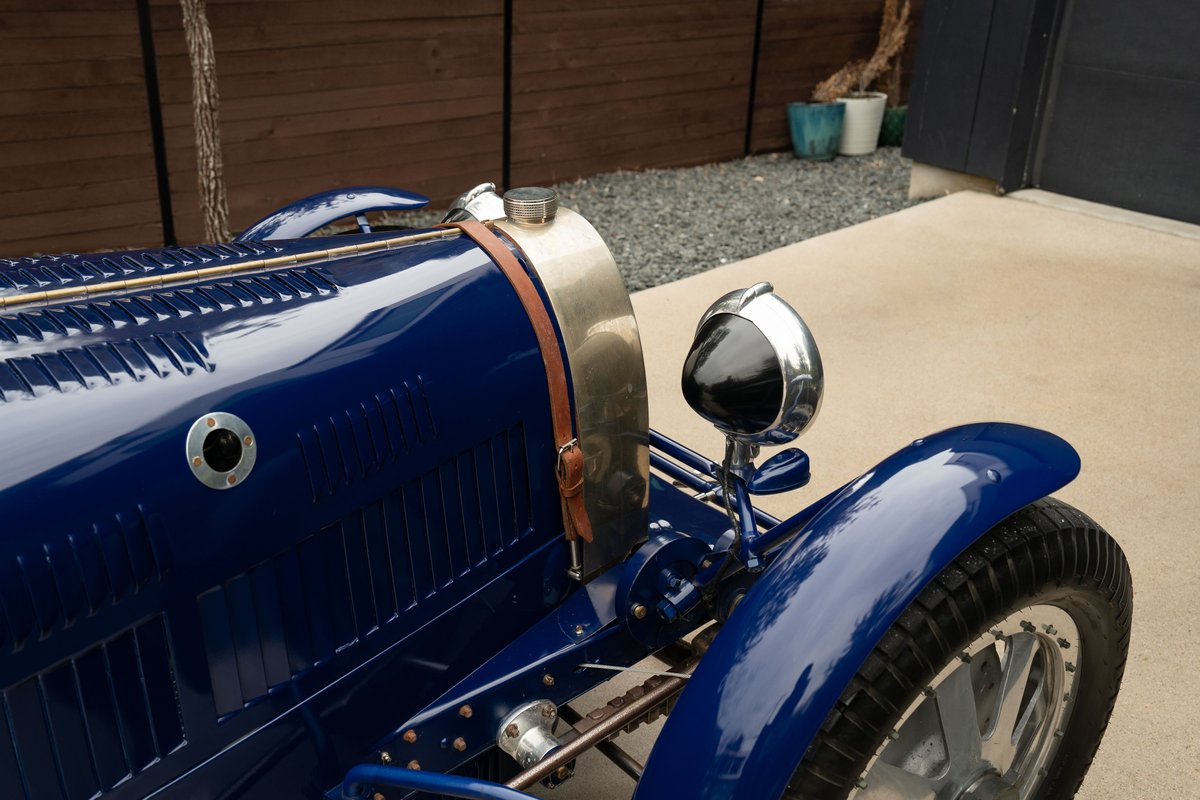 Detail of a blue 1927 Pur Sang Bugatti Type 35, showing the front fender, headlight, and bonnet straps.