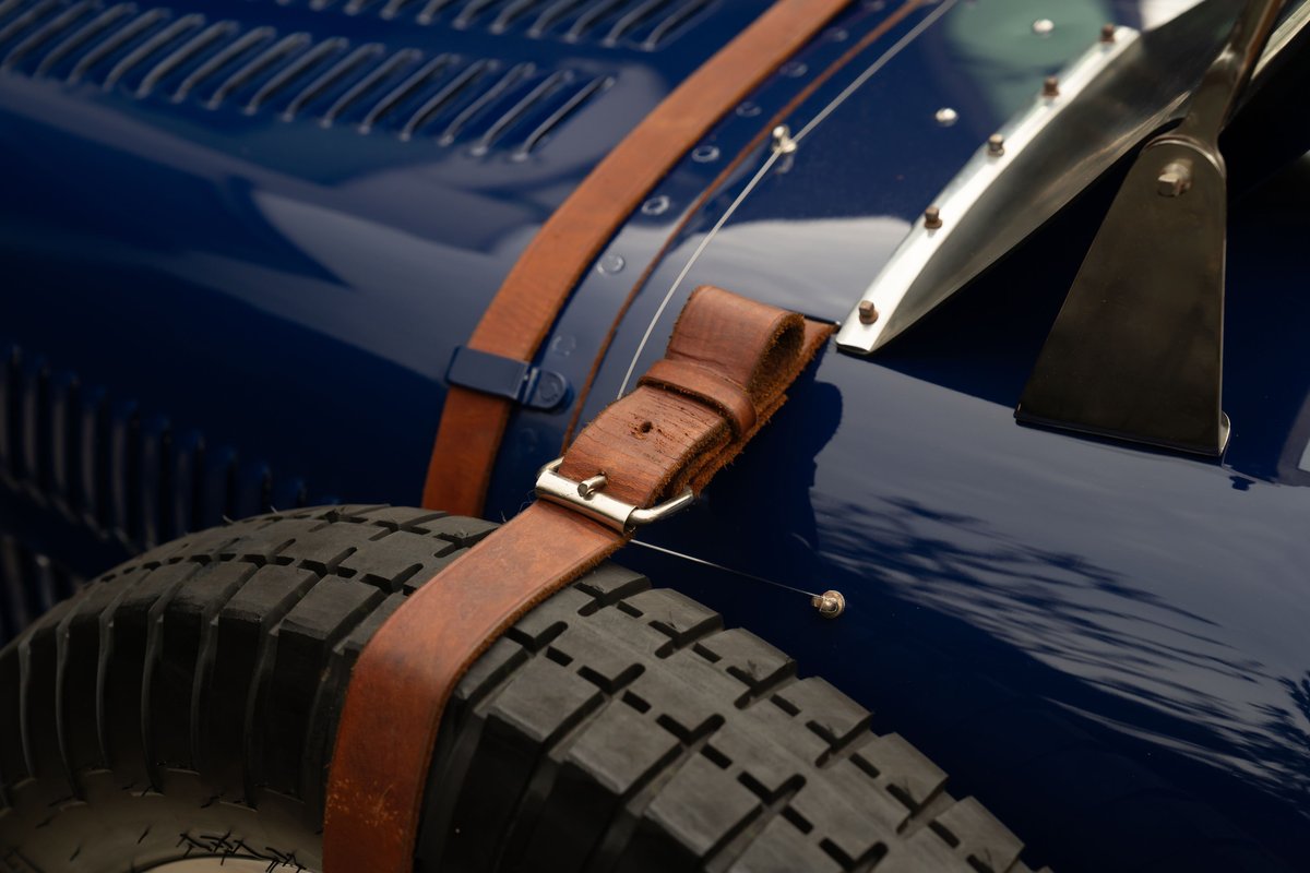 Detail of a blue 1927 Bugatti Type 35's fender, spare tire, and leather hood strap.