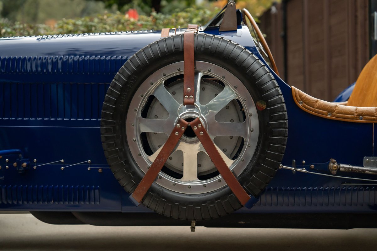 Close-up of a blue 1927 Bugatti Type 35 Pur Sang with a mounted spare tire and leather straps.