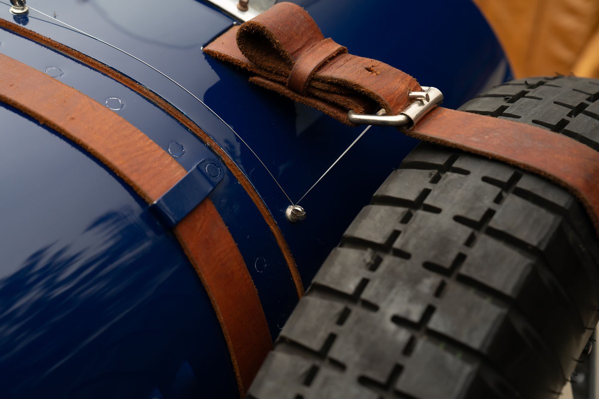Close-up of a blue 1927 Bugatti Type 35 with leather straps holding a spare tire.