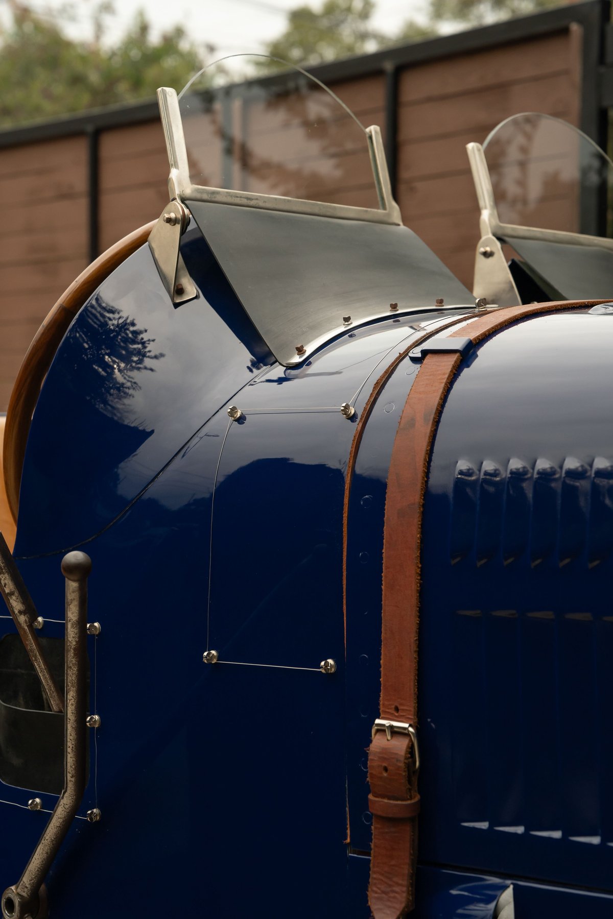 Close-up of a shiny blue 1927 Bugatti Type 35 with twin windscreens & leather straps.