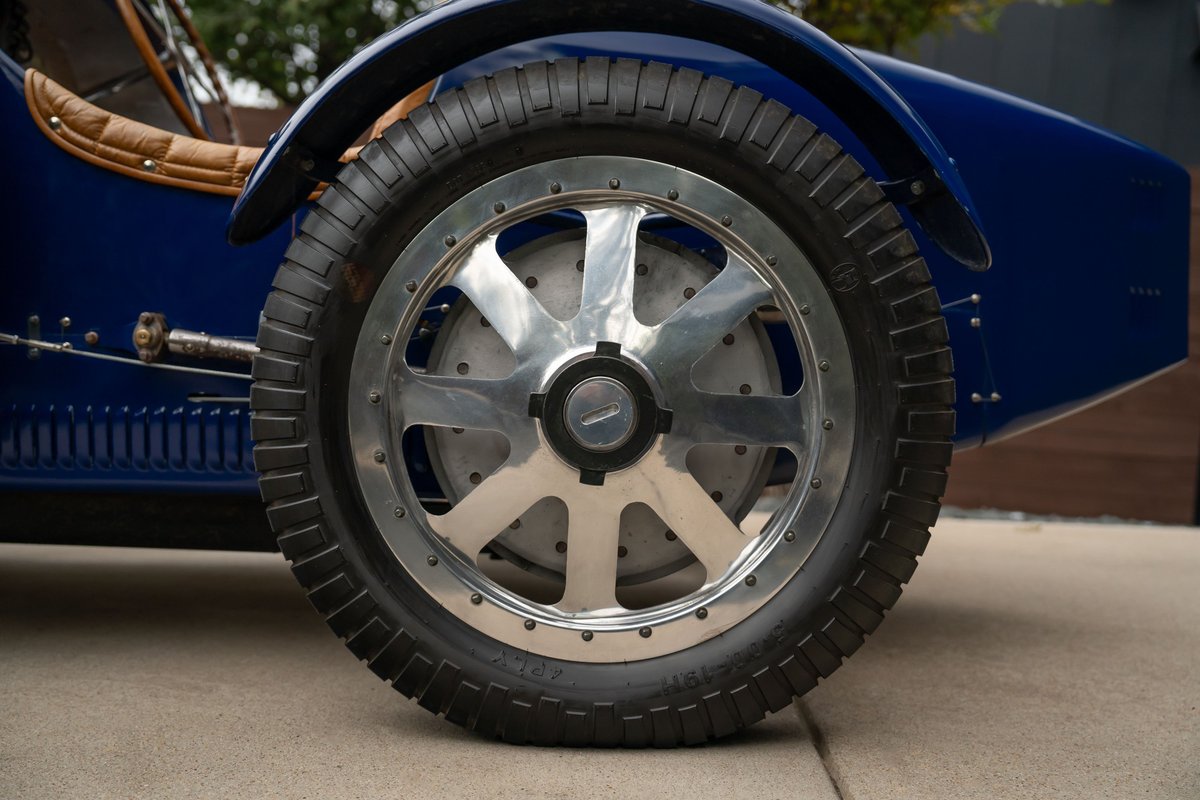 Close-up of a blue 1927 Bugatti Type 35's chrome spoke wheel and ribbed tire.