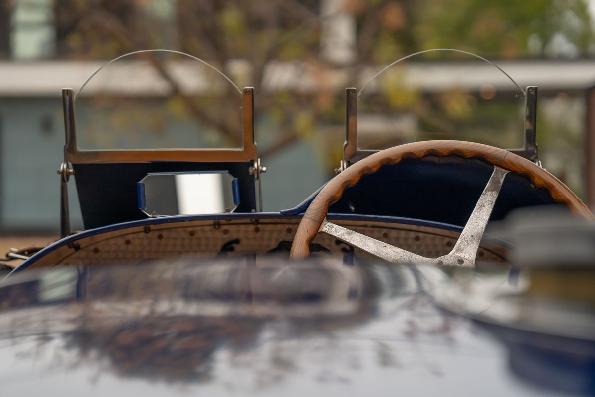 Close-up of a vintage blue Bugatti Type 35 dashboard with wooden steering wheel and dual windscreens.