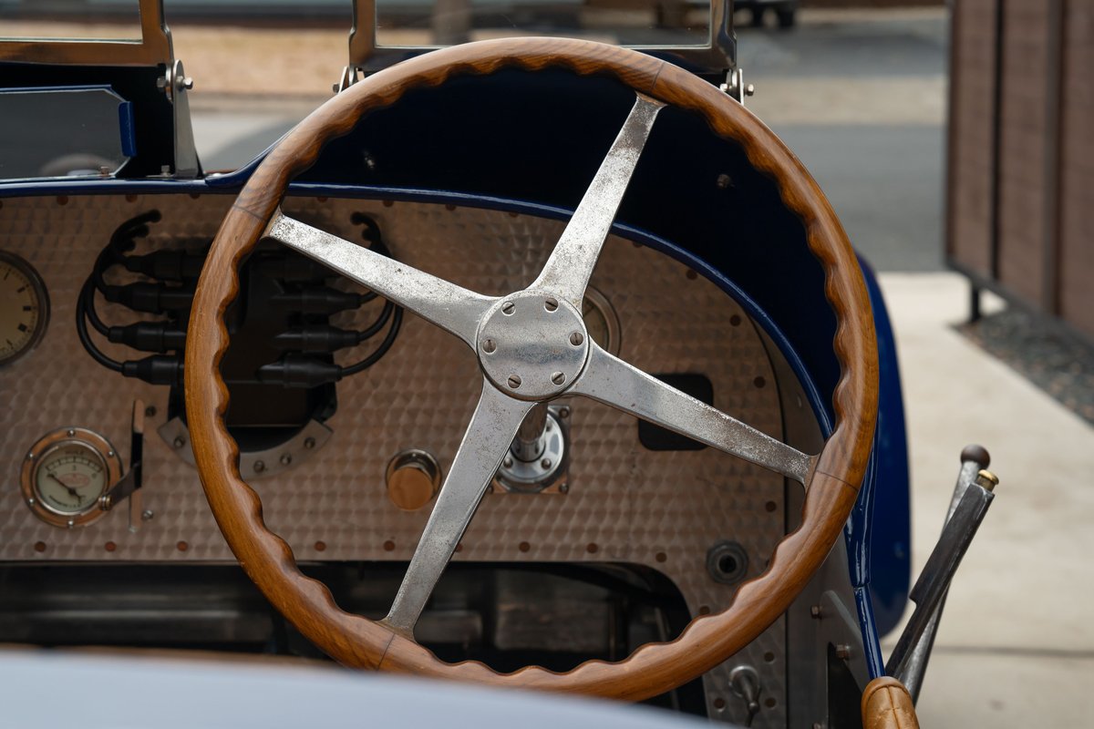 Close-up of a vintage blue 1927 Bugatti Type 35 steering wheel with wooden rim and metal spokes.