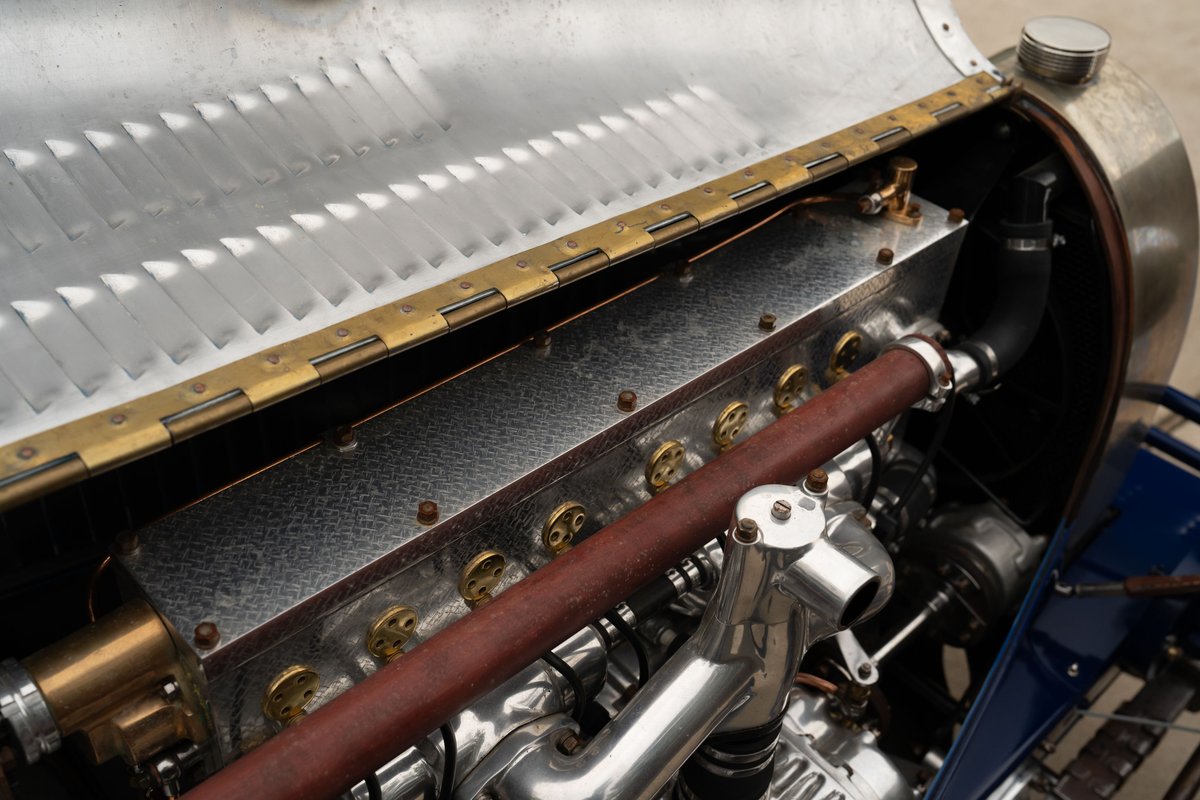 Close-up of a vintage Bugatti Type 35 engine with a red leather-wrapped manifold.