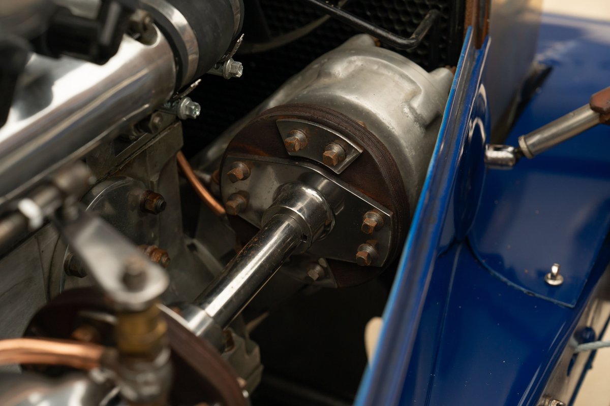 Close-up of a polished metal driveshaft connecting to the engine block of a blue 1927 Bugatti Type 35.