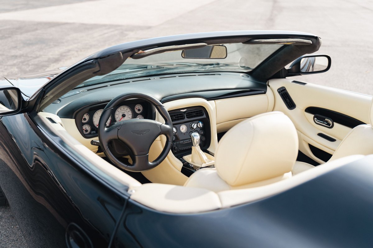 Interior of a black 2003 Aston Martin DB AR1 Zagato convertible with cream leather seats and dashboard.