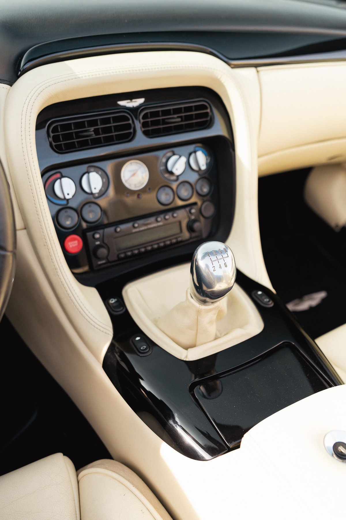 Interior of a black 2003 Aston Martin DB AR1 Zagato showing the manual gear shifter and cream leather trim.