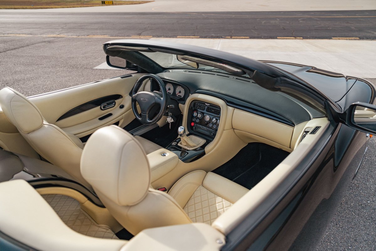 Interior of a black 2003 Aston Martin DB AR1 Zagato convertible with tan quilted leather seats and wood trim.