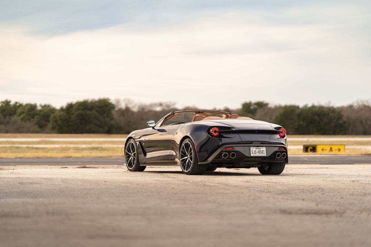Rear view of a dark blue 2018 Aston Martin Vanquish Zagato convertible with tan interior and multi-spoke rims.