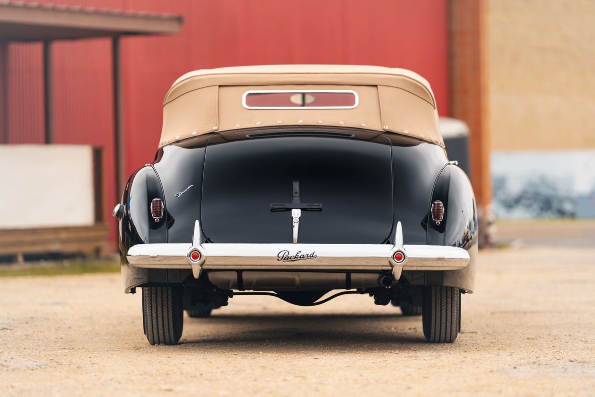 Rear view of a black 1940 Packard Super Eight Convertible with chrome bumper and tan top.