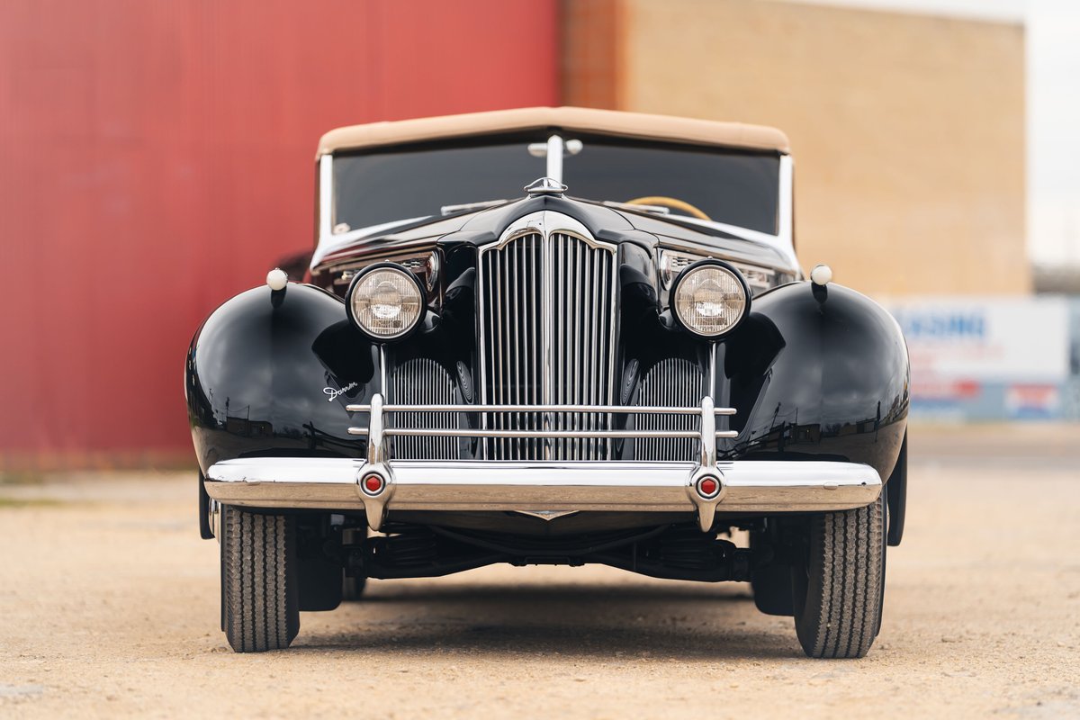 Front view of a black 1940 Packard Super Eight convertible with tan top, chrome grille, and whitewall tires.