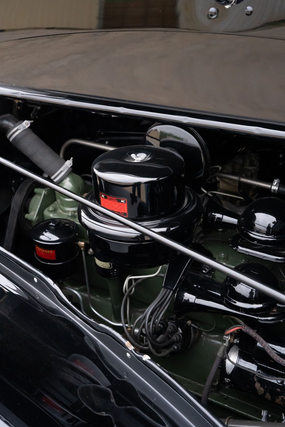 Close-up of the engine bay of a black 1940 Packard Super Eight One-Eighty, featuring its vintage air cleaner and engine block.