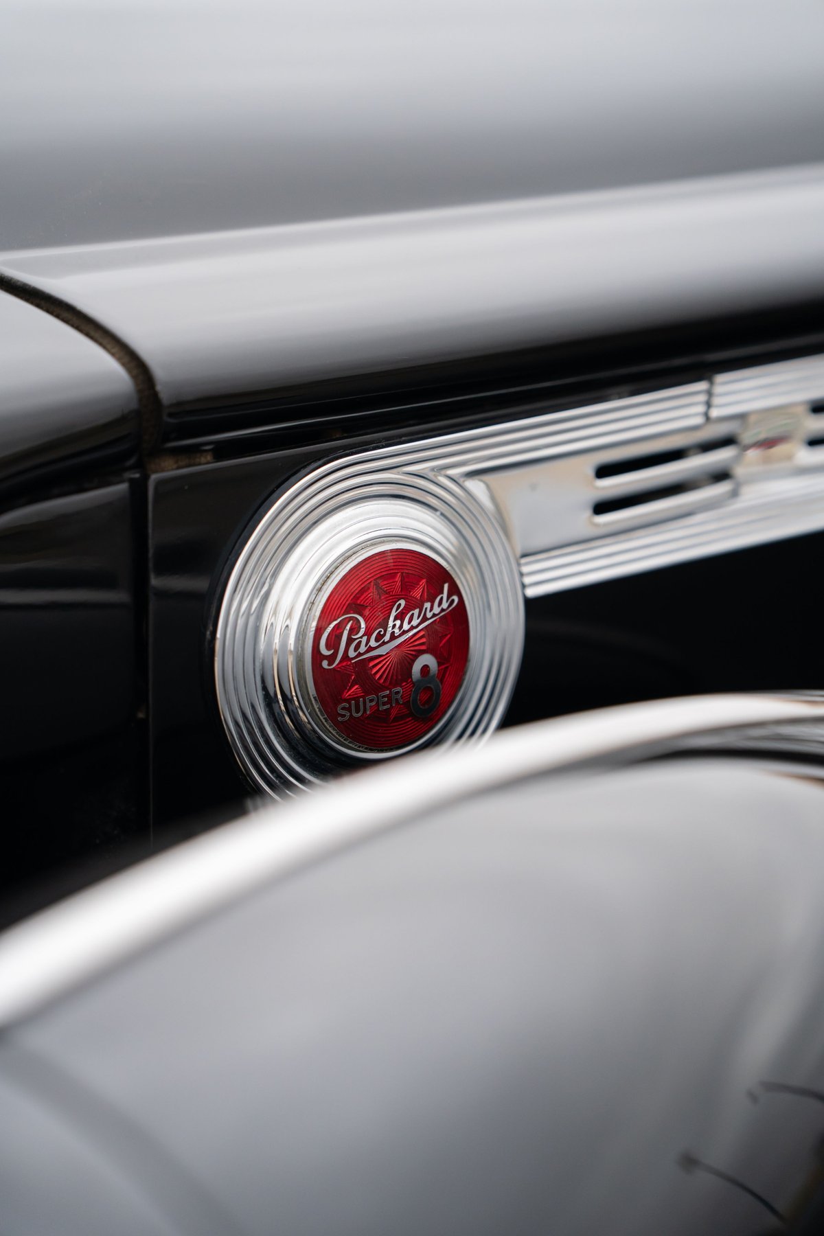 Close-up of a black 1940 Packard Super Eight's circular, red Packard Super 8 emblem and chrome trim.