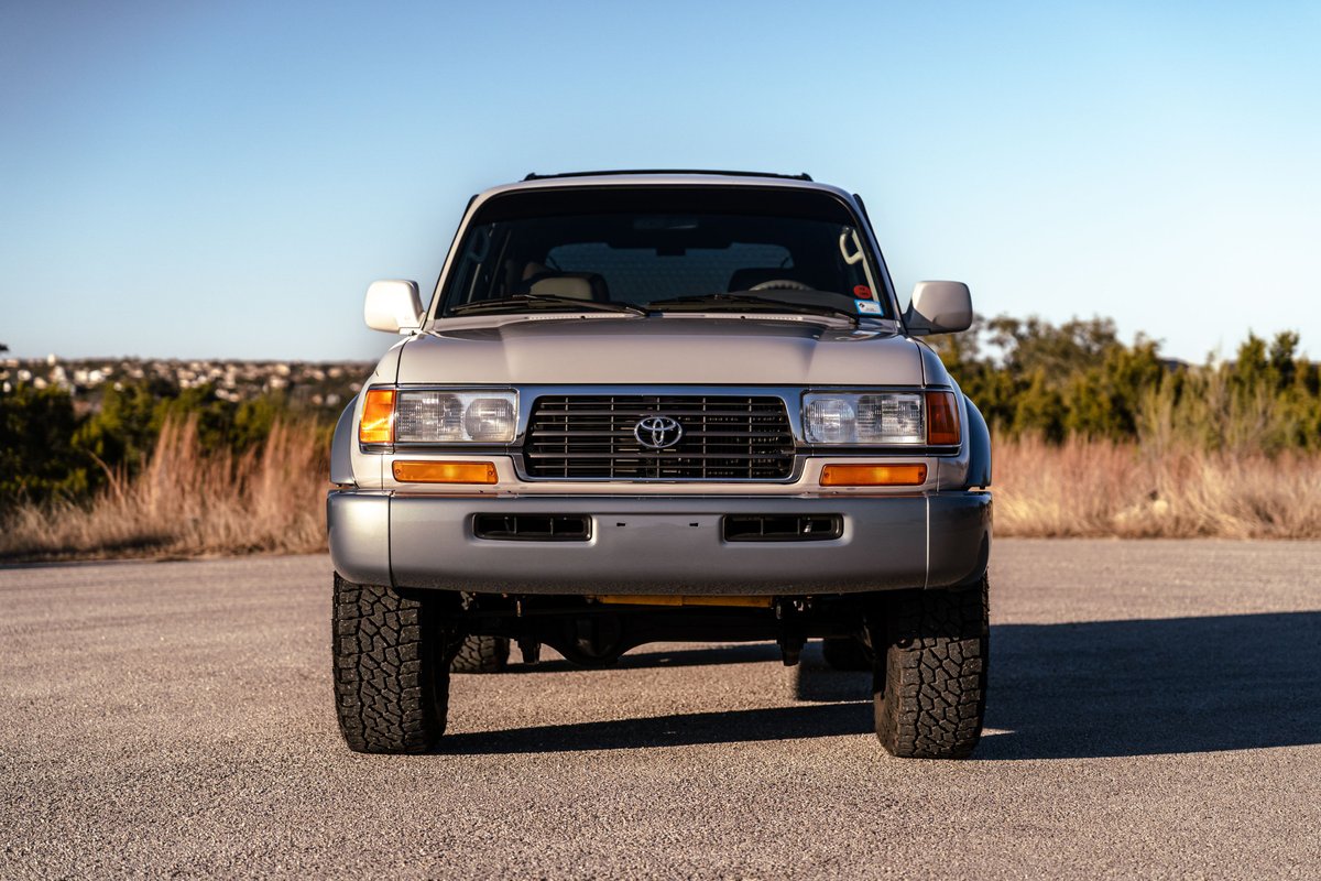 Front view of a Desert Dune Metallic 1997 Toyota Land Cruiser FJ80 with all-terrain tires.