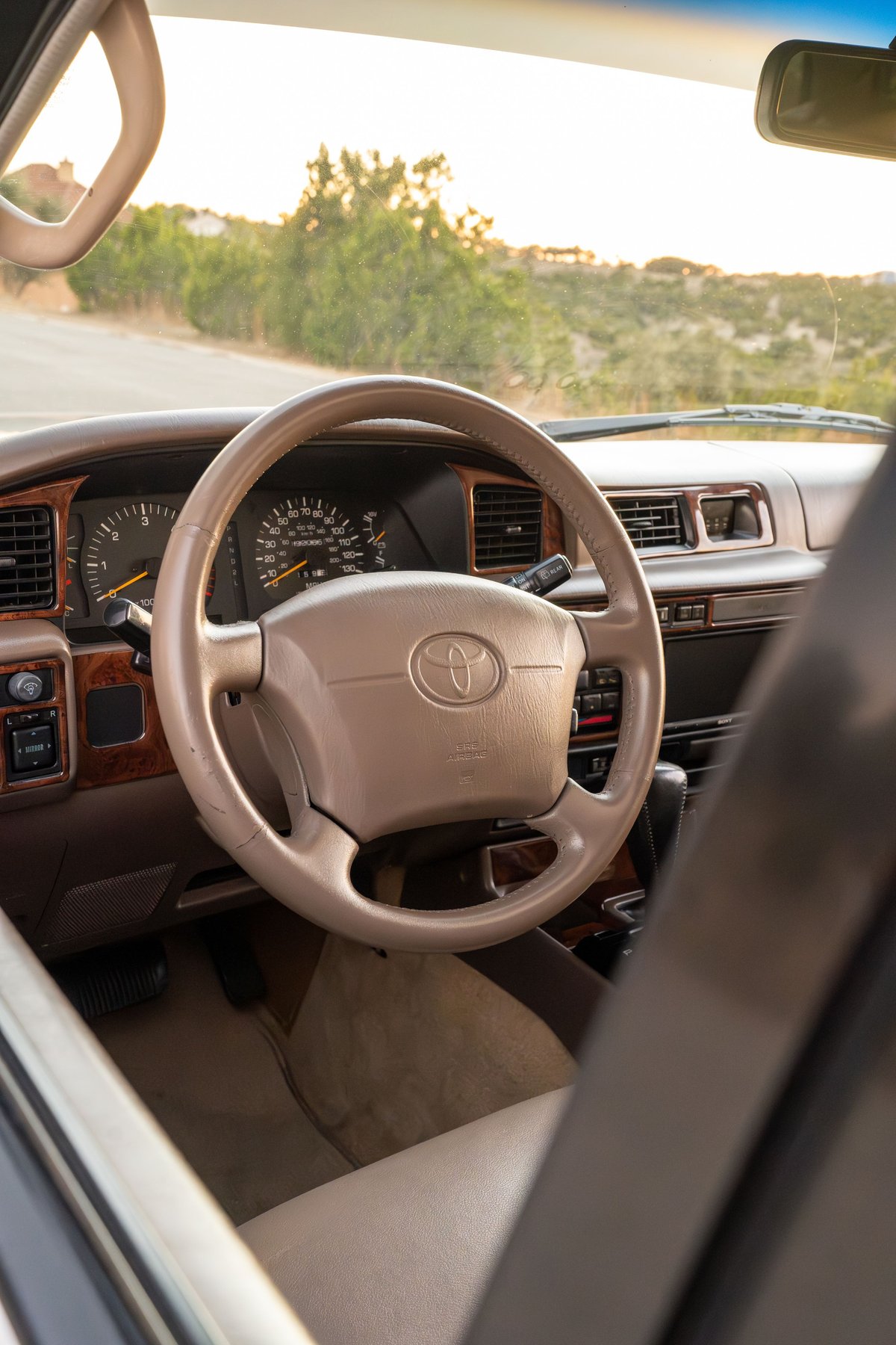 Interior of a Desert Dune Metallic 1997 Toyota Land Cruiser FJ80 showing the tan steering wheel, dashboard, and wood trim.