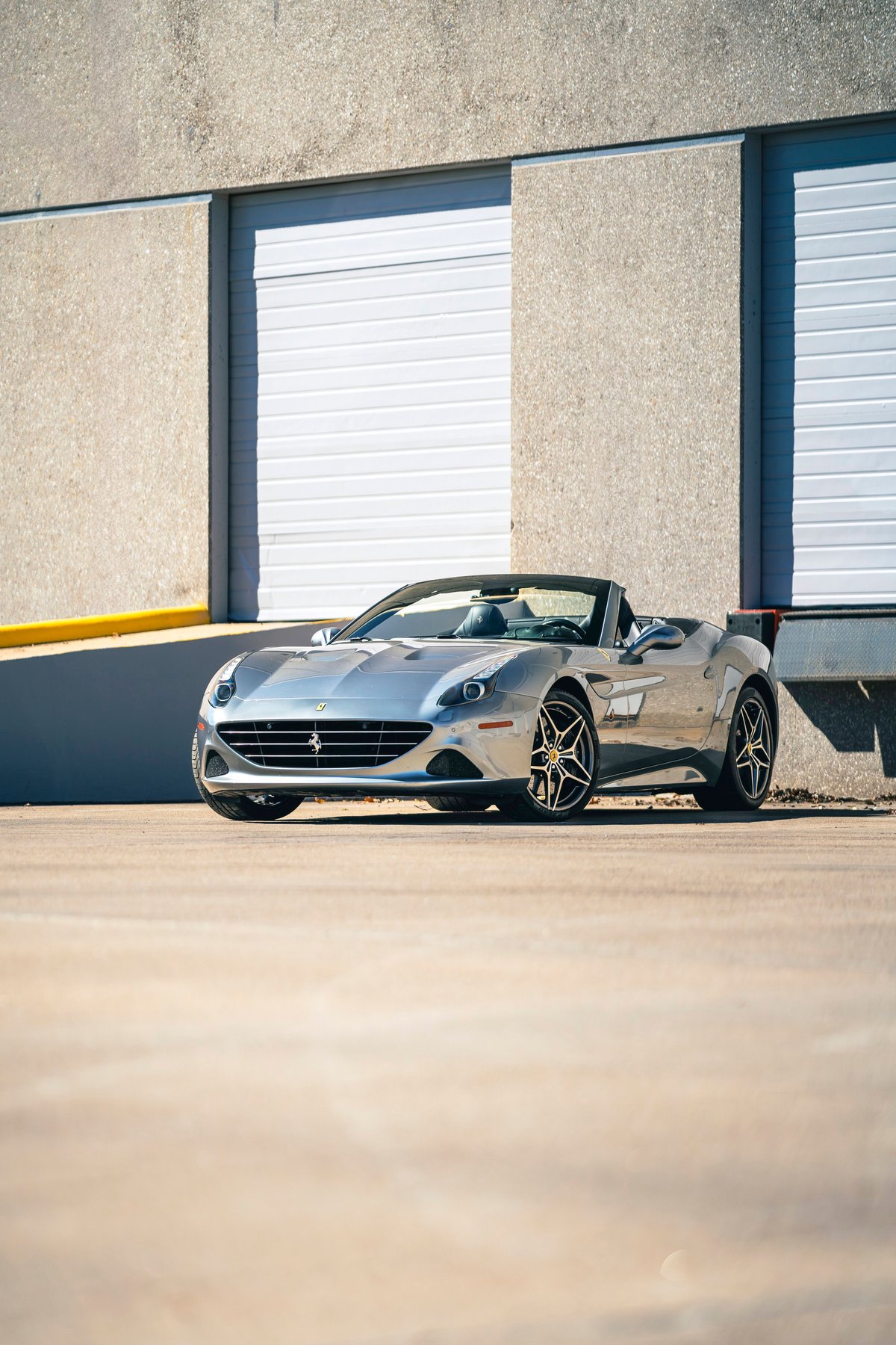 Silver 2016 Ferrari California T convertible with black multi-spoke rims parked outside a building.