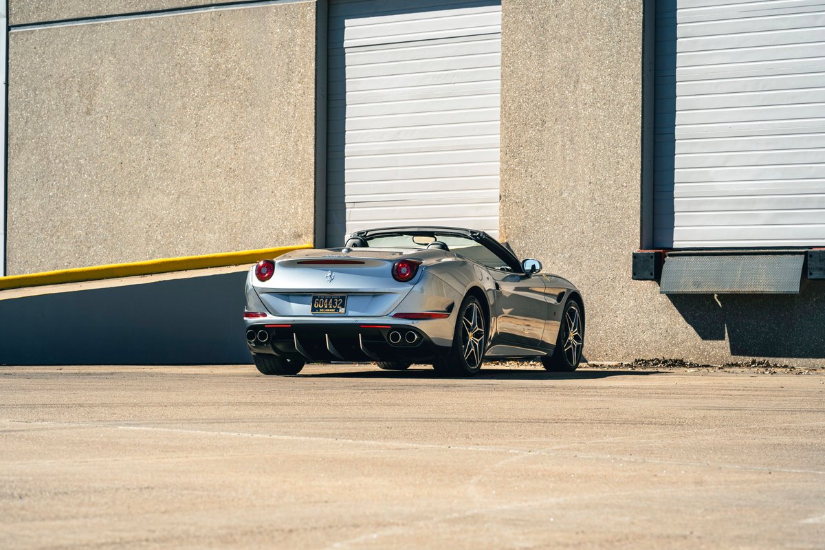 Silver 2016 Ferrari California T convertible with dark multi-spoke rims parked by a loading dock.